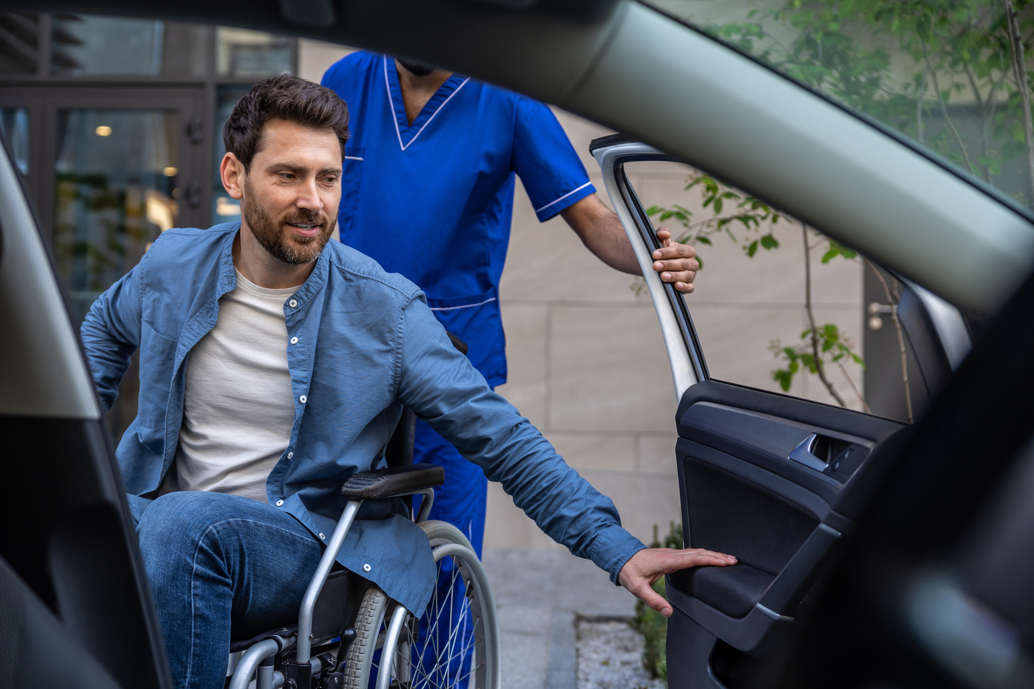 Disabled man getting on a car, male nurse helping him