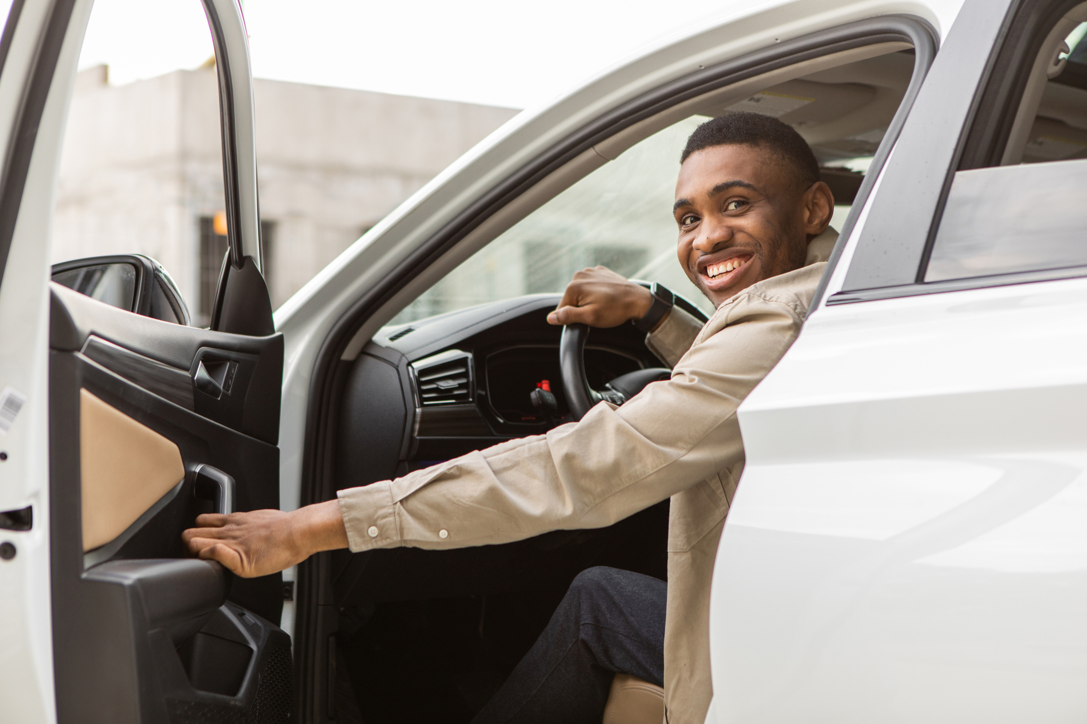 Smiling man sitting in the car, getting in or out of the car, holding the door open, looking at the camera